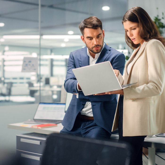Two employees standing, holding a laptop, and discussing steps and measures they can use to minimize downtime.